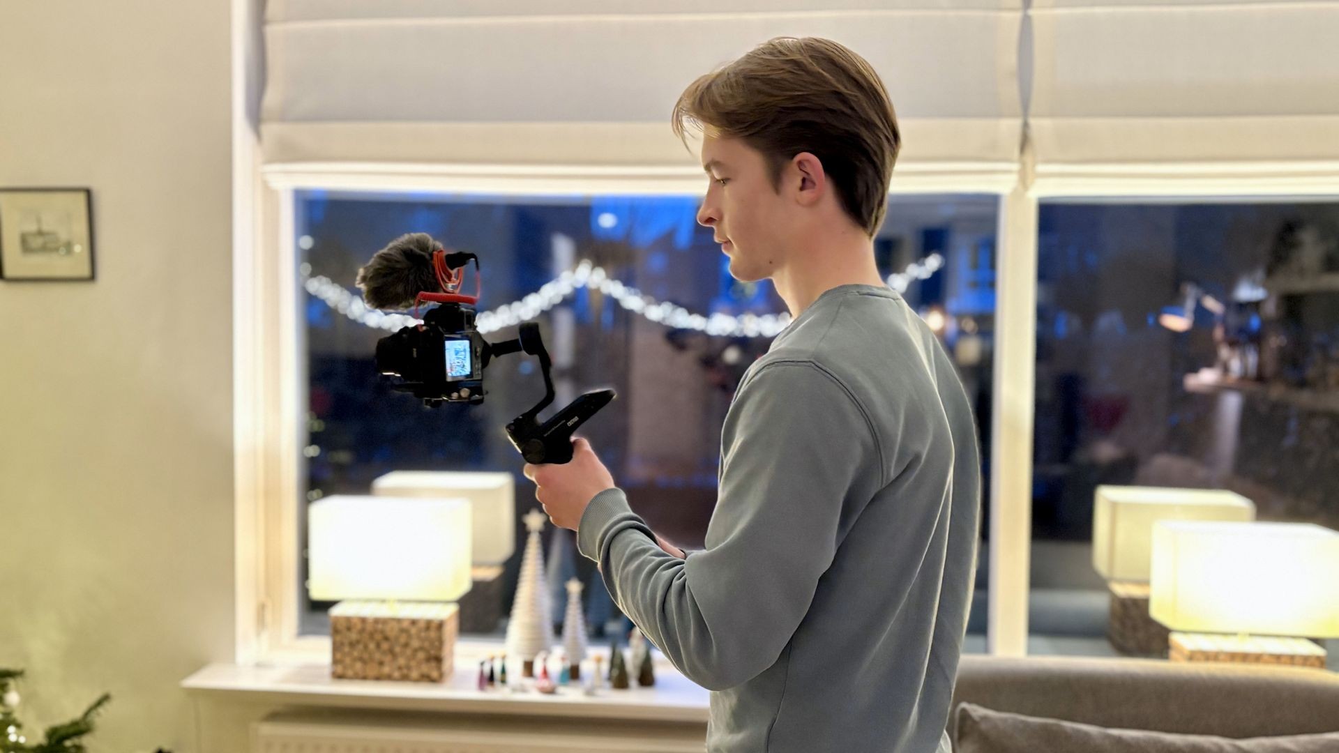 Person holding a camera on a gimbal in a cozy room with holiday decorations and lights.